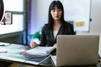 Giovane ragazza segue una lezione a distanza seduta alla scrivania con davanti a lei un computer portatile e uno smartphone usato come webcam