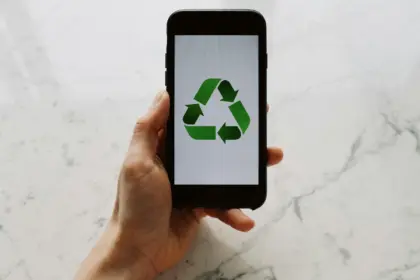 Mano in primo piano sorregge uno smartphone che mostra il simbolo universale del riciclo con tre frecce verdi che formano un triangolo
