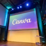 Palco di un teatro allestito per un evento di formazione con un maxischermo che mostra il logo di Canva