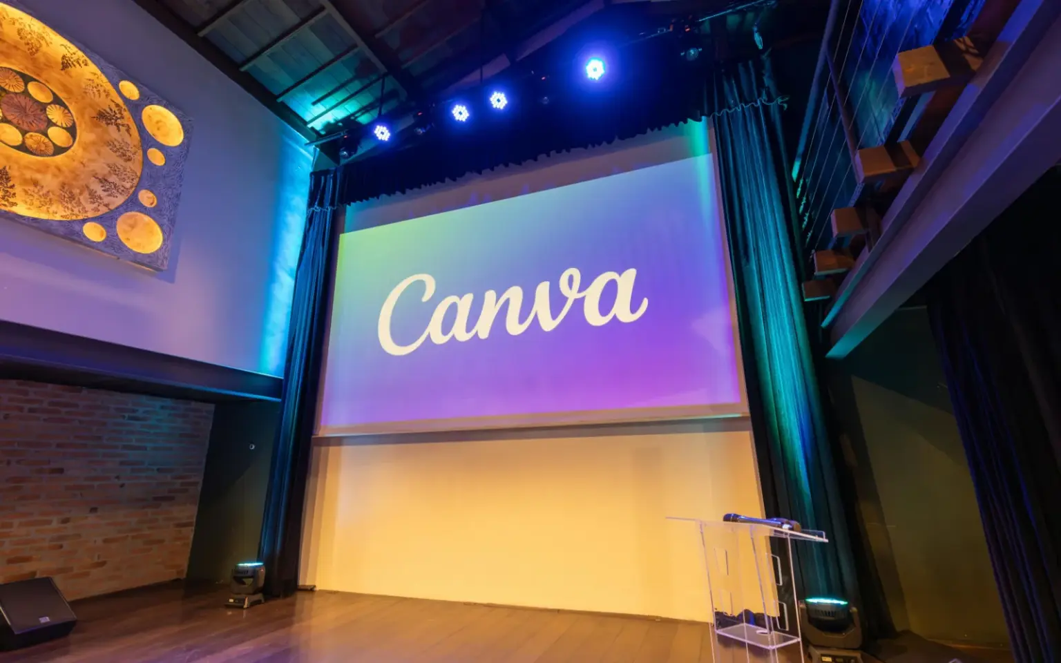 Palco di un teatro allestito per un evento di formazione con un maxischermo che mostra il logo di Canva