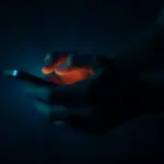 Mani che digitano sullo schermo di uno smartphone in un ambiente chiuso e completamente buio