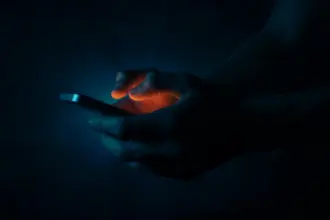 Mani che digitano sullo schermo di uno smartphone in un ambiente chiuso e completamente buio
