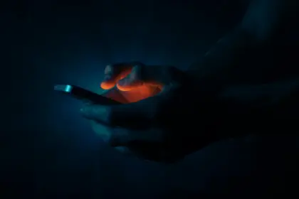 Mani che digitano sullo schermo di uno smartphone in un ambiente chiuso e completamente buio