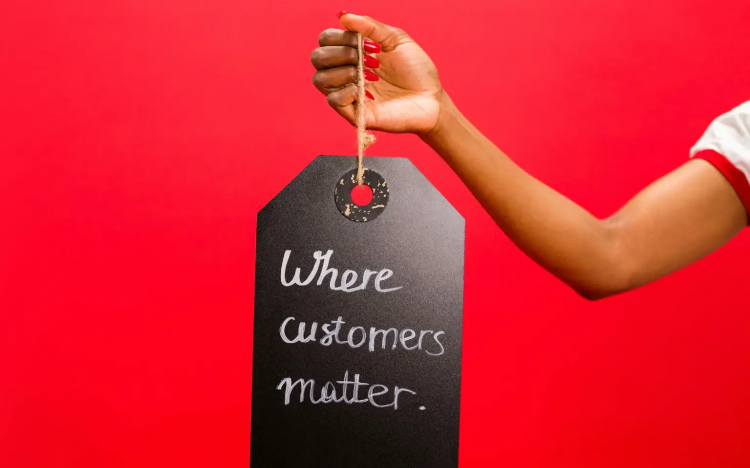 Mano femminile sostiene una lavagna nera con la frase "Where customers matters" su una parete colorata di rosso