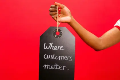 Mano femminile sostiene una lavagna nera con la frase "Where customers matters" su una parete colorata di rosso