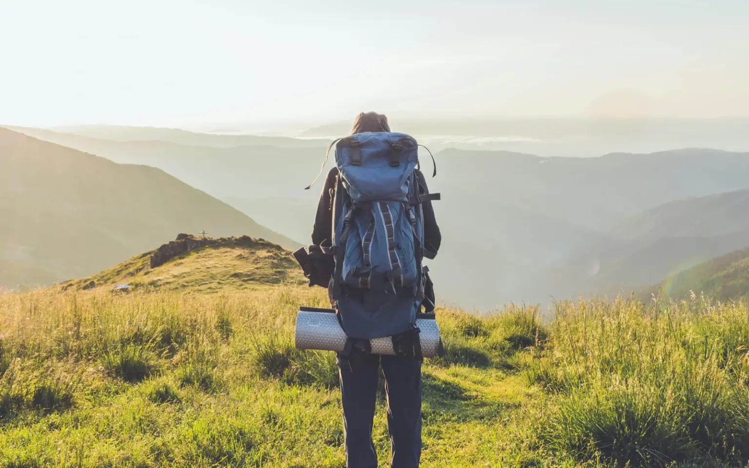 Persona con abbigliamento tecnico e zaino da trekking visto di spalle su un sentiero in mezzo agli appennini