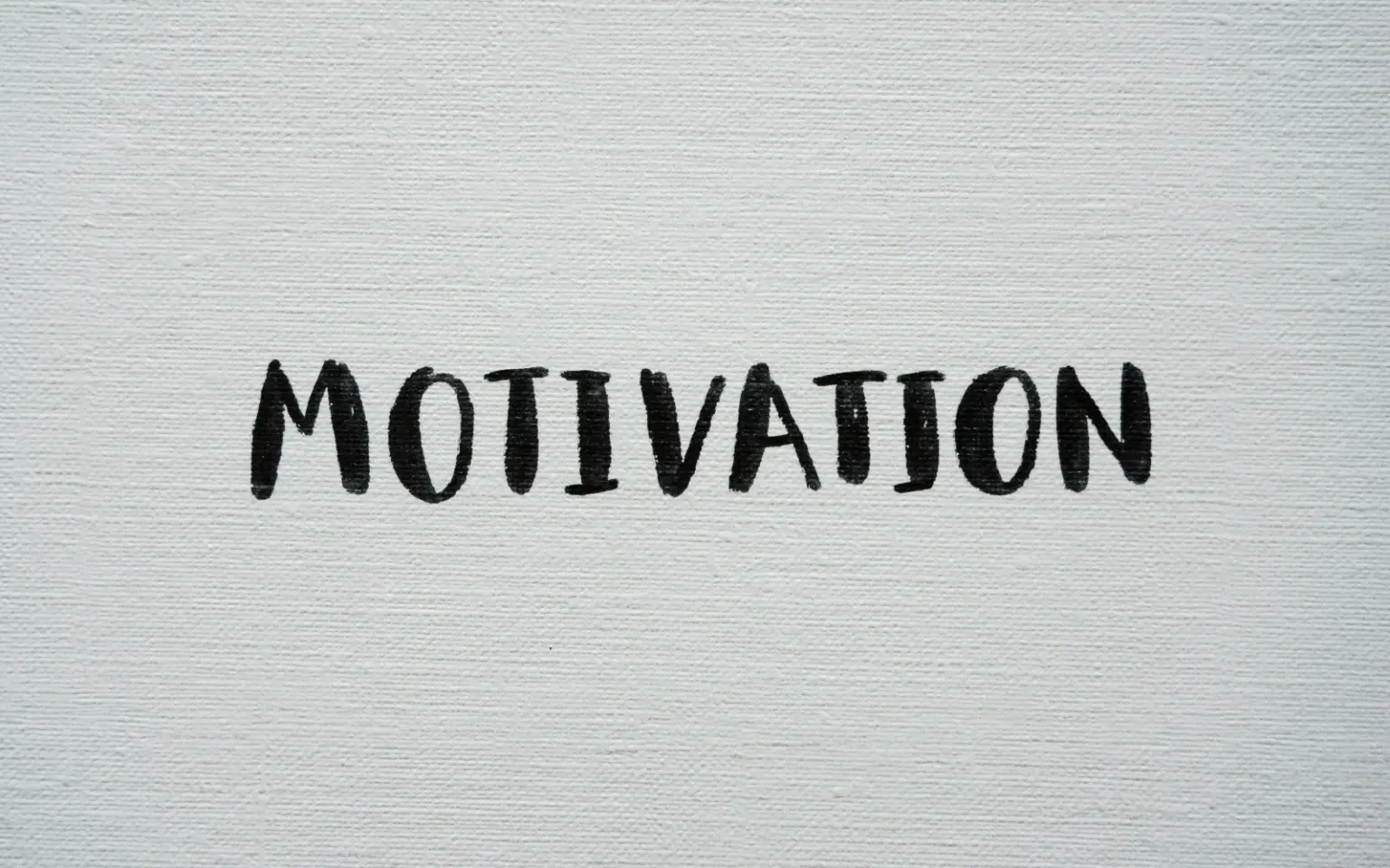 Scritta "Motivation" scritta a mano con un pennello a tempera nera su una tela canvas bianca